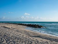 a long stretch of sandy beach covered with sand and water beneath a blue sky with clouds