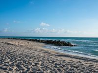 a long stretch of sandy beach covered with sand and water beneath a blue sky with clouds