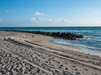 a long stretch of sandy beach covered with sand and water beneath a blue sky with clouds