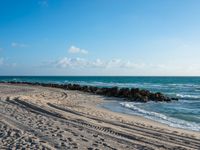 a long stretch of sandy beach covered with sand and water beneath a blue sky with clouds