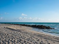 a long stretch of sandy beach covered with sand and water beneath a blue sky with clouds