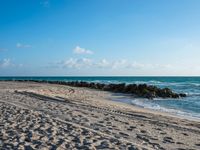 a long stretch of sandy beach covered with sand and water beneath a blue sky with clouds