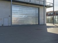 a guy riding a skateboard past a garage door on the street near buildings in the sunshine