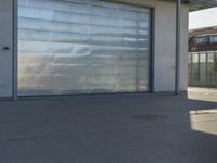 a guy riding a skateboard past a garage door on the street near buildings in the sunshine