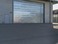 a guy riding a skateboard past a garage door on the street near buildings in the sunshine