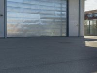 a guy riding a skateboard past a garage door on the street near buildings in the sunshine