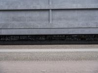 there is a person standing under an overpass on the sidewalk by a building and there is a bike