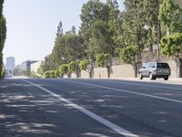 the trees on either side of the road have long shadows over it with an area for cars to drive by