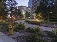 a street and some plants near some buildings at night time, at dusk, with a fire hydrant at the center