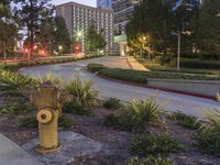 a street and some plants near some buildings at night time, at dusk, with a fire hydrant at the center