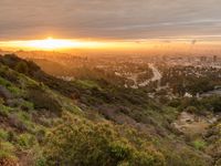 view from a hillside of a valley with a beautiful sunset on the horizon and a city in the background