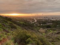 view from a hillside of a valley with a beautiful sunset on the horizon and a city in the background