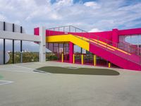 a colorful basketball court with a big stairwell on one floor and yellow railings on the other side