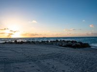 the sun sets on an empty beach with rocks and sand in front of it,