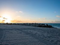 the sun sets on an empty beach with rocks and sand in front of it,