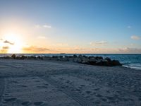 the sun sets on an empty beach with rocks and sand in front of it,