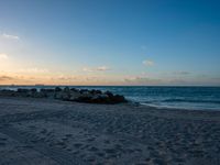 the sun sets on an empty beach with rocks and sand in front of it,