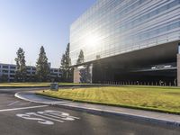 a modern glass building sits on the corner of a large green field in front of trees