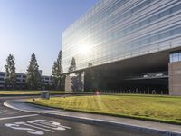 a modern glass building sits on the corner of a large green field in front of trees