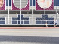 two people walking on the side of a road by a building with advertisements on it