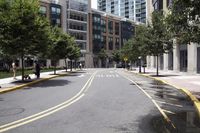 people are crossing the street in an area with many tall buildings and trees on both sides