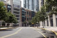 people are crossing the street in an area with many tall buildings and trees on both sides