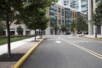 people are crossing the street in an area with many tall buildings and trees on both sides