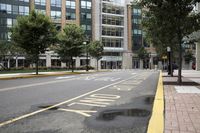 people are crossing the street in an area with many tall buildings and trees on both sides