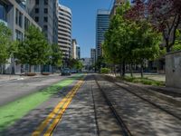 the green paint is painted on a bike path in front of an office building and large, trees