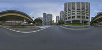 a fisheye lens photograph of a city street with tall buildings in the background and a person riding a skateboard on the road at the corner