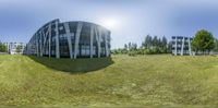 a field with a building and some trees in the background and a blurry photo of the reflection of the sky on the windows