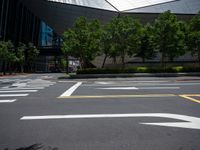 a city street with white arrows marked in the parking spaces on both sides and trees, along with an outdoor seating area with glass buildings