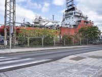 the large ship is in the background with traffic on the road nearby, and other buildings, bushes, trees and buildings