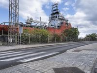 the large ship is in the background with traffic on the road nearby, and other buildings, bushes, trees and buildings