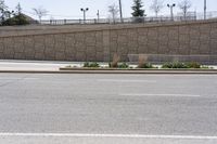 a person on a skateboard going on a city street near a large wall and a stone fence