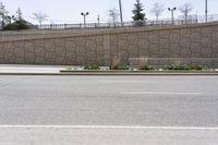 a person on a skateboard going on a city street near a large wall and a stone fence