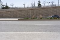 a person on a skateboard going on a city street near a large wall and a stone fence