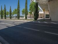 a car sitting at an empty street underneath a overpass overhang that contains a train stop, and cars and a pedestrian