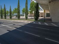 a car sitting at an empty street underneath a overpass overhang that contains a train stop, and cars and a pedestrian