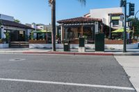 the sidewalk has benches and umbrellas on it as well as palm trees in front of a restaurant