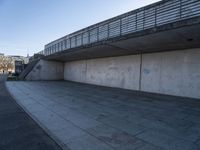 a skateboard sits outside a concrete structure that is next to a street area with a bench