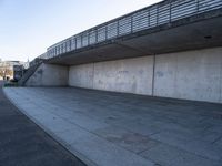 a skateboard sits outside a concrete structure that is next to a street area with a bench