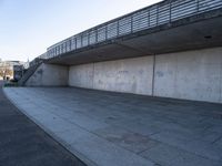 a skateboard sits outside a concrete structure that is next to a street area with a bench