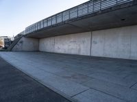 a skateboard sits outside a concrete structure that is next to a street area with a bench