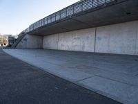 a skateboard sits outside a concrete structure that is next to a street area with a bench