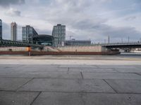 an empty street in the city next to a bridge and city buildings under a cloudy sky