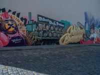 some colorful street murals on a side walk and a brick ground, a person on a skateboard near some buildings