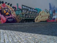 some colorful street murals on a side walk and a brick ground, a person on a skateboard near some buildings