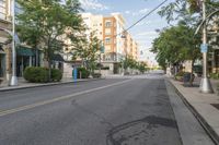 a deserted street lined with apartment buildings and trees on either side of the road and a single street sign on the opposite corner