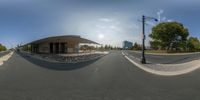 a fisheye view of a street and sky from the intersection of a roundabout with cars passing by